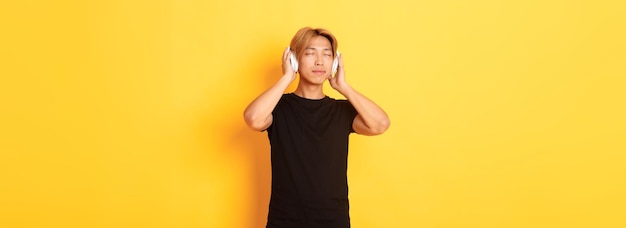 Détendu et heureux, un beau mec asiatique ferme les yeux de satisfaction tout en écoutant de la musique sans fil
