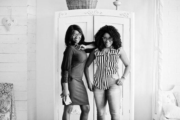 Photo gratuite deux amies africaines portent des lunettes posées à l'intérieur de la salle blanche contre une armoire rustique