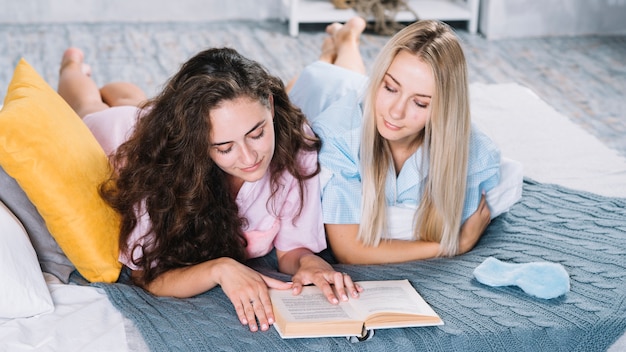 Deux amies allongées sur le lit, livre de lecture