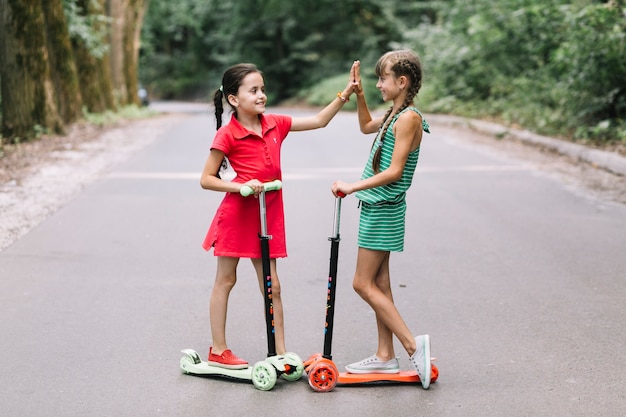 Deux amies debout sur un scooter donnant cinq geste haut sur la route