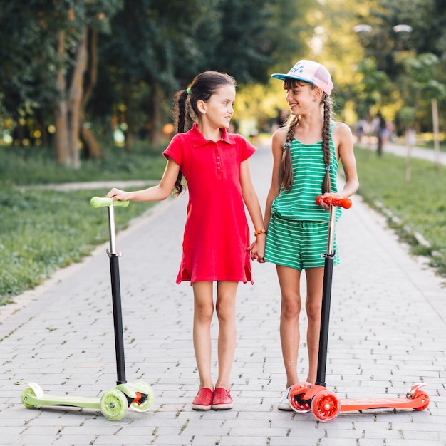 Photo gratuite deux amies debout sur le trottoir avec leurs scooters