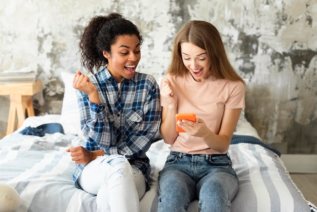 Deux amies sur le lit à la recherche de smartphone