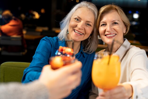 Deux amies plus âgées buvant dans un restaurant avec leur ami masculin