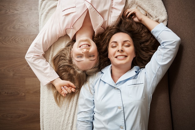 Deux amis allongés sur un canapé en pyjama confortable avec les yeux fermés, souriant et relaxant
