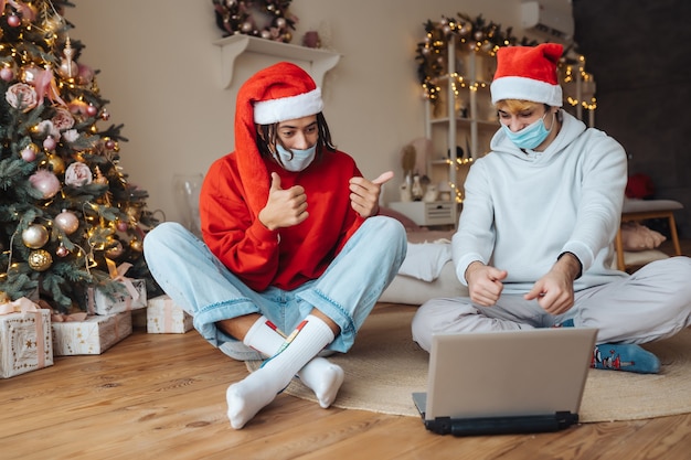 Deux amis en bonnet de Noel près de l'ordinateur portable interagissent via des appels vidéo