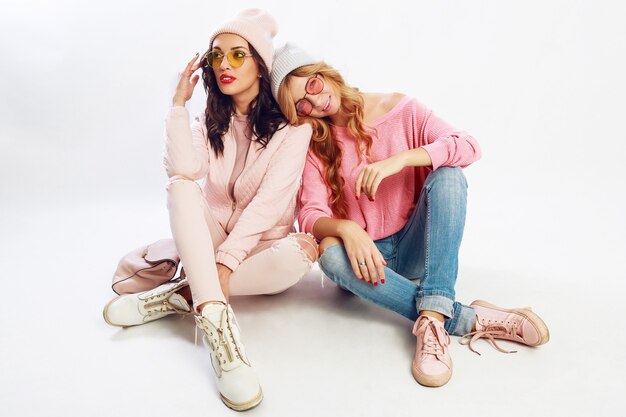 Deux amis fatigués se détendre sur un sol blanc en studio. Jolie tenue rose. Des chaussures élégantes.