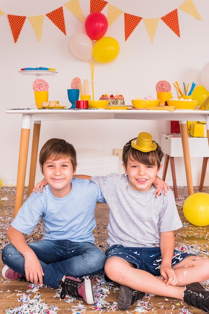 Photo gratuite deux amis hommes souriants, assis avec des confettis sur le plancher de bois franc