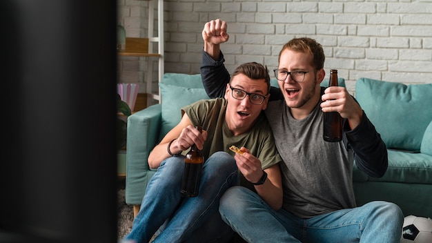 Deux amis masculins joyeux, regarder le sport à la télévision et boire de la bière