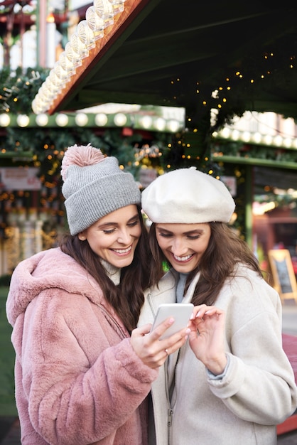 Deux amis parcourant un téléphone mobile sur un marché de Noël