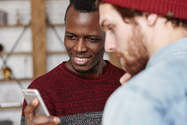 Deux amis de races différentes s'amusant à l'intérieur, en utilisant un gadget électronique