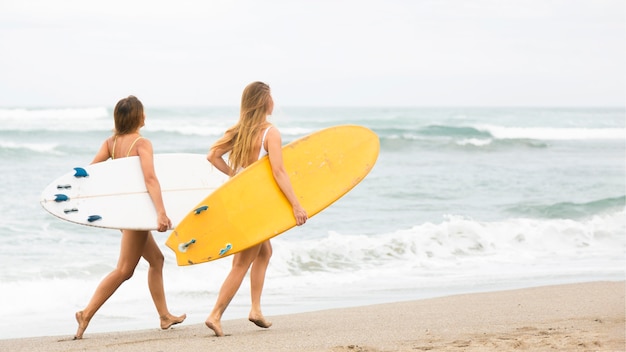 Photo gratuite deux amis souriants s'exécutant sur la plage avec des planches de surf
