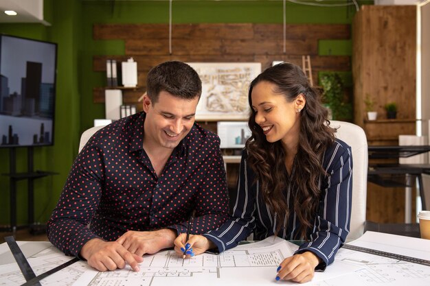 Deux architectes souriants sont assis à une table et discutent d'un nouveau projet. Bureau moderne et imprimé bleu