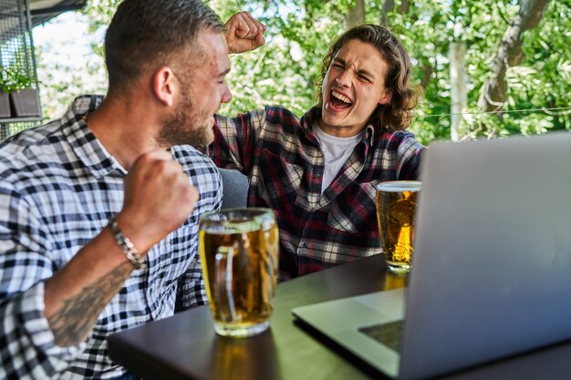 Deux beaux hommes regardent le football dans un pub et boivent de la bière.
