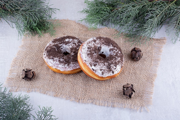 Deux beignets sur un morceau de tissu parmi les branches de pin sur fond blanc.