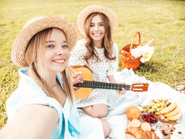 Deux belle jeune femme hipster en robe d'été à la mode et chapeaux. Femmes insouciantes faisant un pique-nique à l'extérieur.