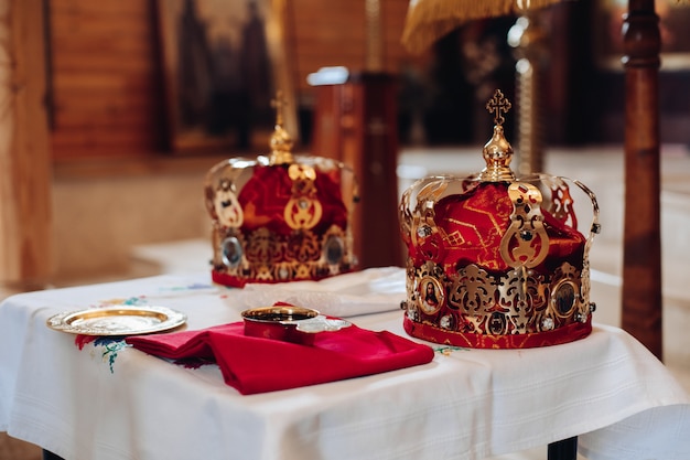 Deux belles couronnes avec de l'or et du tissu rouge se tiennent sur une table dans l'église avant le baptême du bébé