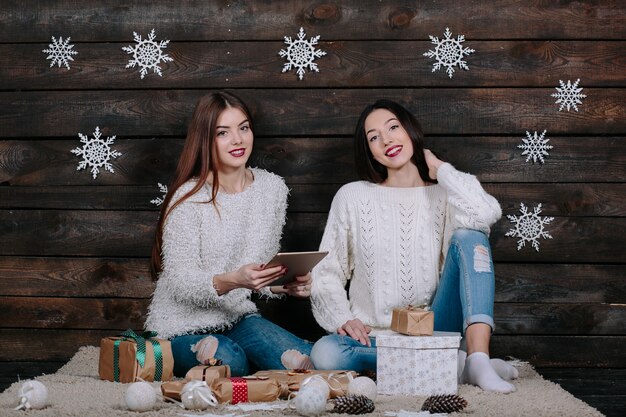 Deux belles femmes assises sur le sol avec une tablette, entre les cadeaux pour Noël