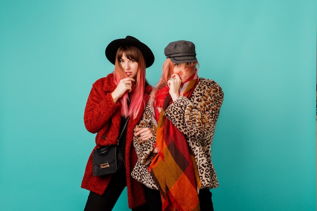 Deux belles femmes en manteaux de fausse fourrure élégants et écharpe en laine posant sur un mur turquoise