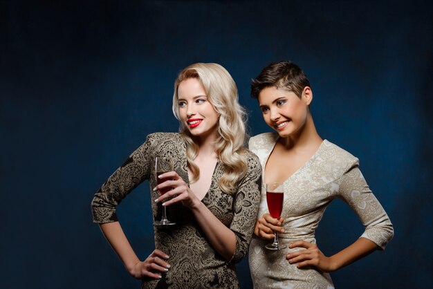 Deux belles femmes en robes de soirée souriant, tenant des verres à vin