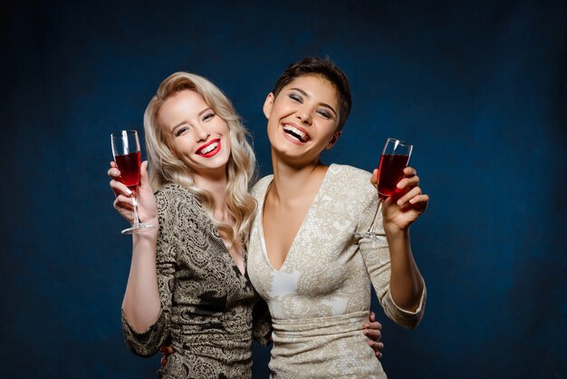 Deux belles femmes en robes de soirée souriant, tenant des verres à vin