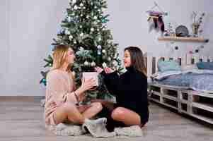 Photo gratuite deux belles filles amies portent un pull chaud et des guêtres jambières contre l'arbre du nouvel an avec décoration de noël vacances en studio portrait de fille blonde et brune