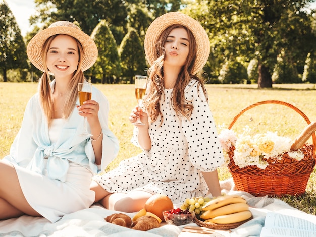 Deux belles jeunes femmes hipster souriantes en robe d'été et chapeaux. Femmes insouciantes faisant un pique-nique à l'extérieur.