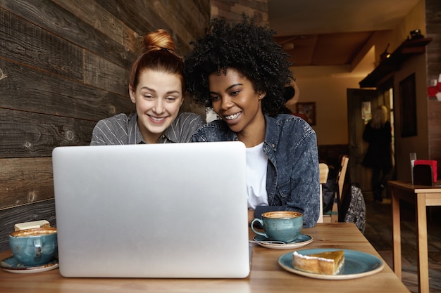 Photo gratuite deux belles jeunes femmes de races différentes, assis devant un ordinateur portable ouvert