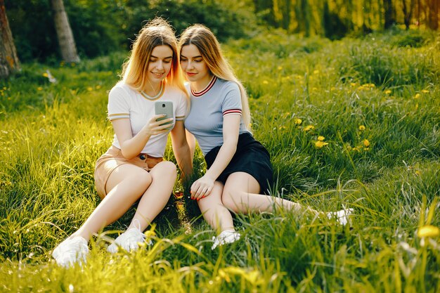 deux belles jeunes filles belles avec des cheveux blonds brillants et une jupe et assis avec un téléphone