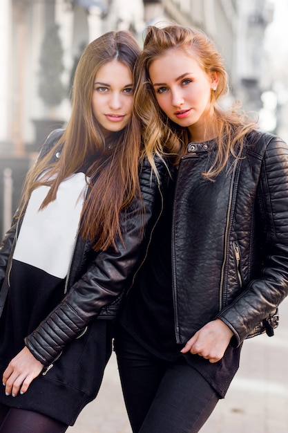 Deux belles jeunes filles posant ensemble à l'extérieur. Ambiance urbaine de style de vie. Fond de centre-ville. Meilleurs amis portant une tenue d'automne décontractée noire.