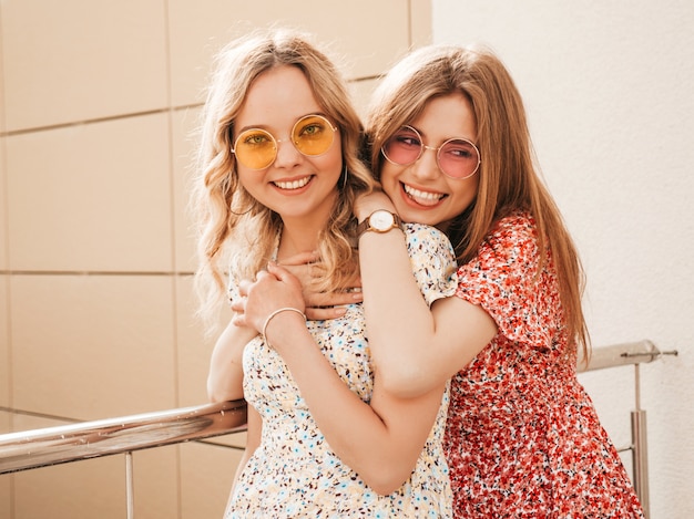 Deux belles jeunes filles souriantes hipster en robe d'été à la mode.Des femmes insouciantes sexy posant sur le fond de la rue en chapeaux. Des mannequins positifs s'amusant et se serrant dans leurs bras.