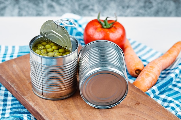 Deux boîtes de pois verts bouillis, légumes et nappe sur une table blanche et en marbre.