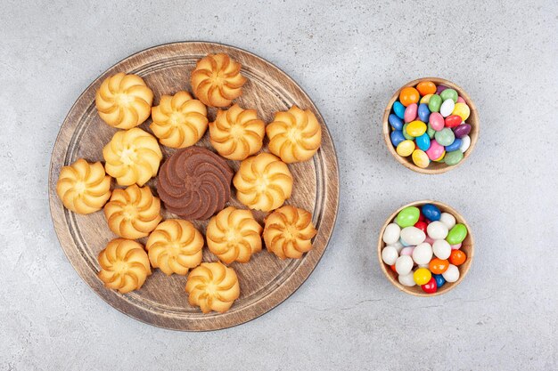 Deux bols de bonbons à côté d'un arrangement décoratif de biscuits sur planche de bois sur une surface en marbre.