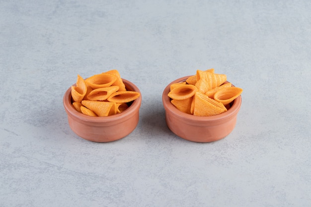 Deux bols de chips croustillantes en forme de triangle sur fond de pierre.