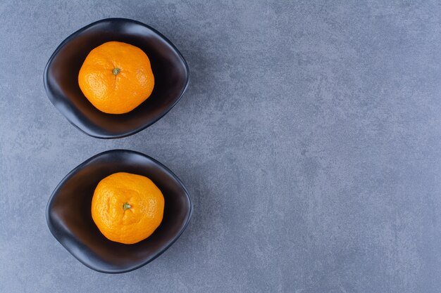 Deux bols d'oranges, sur la surface sombre
