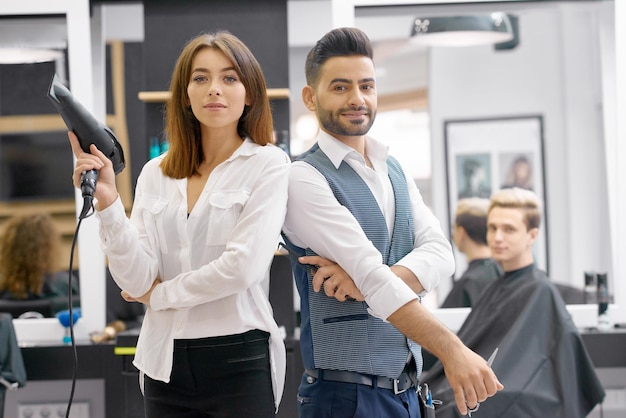 Photo gratuite deux coiffeurs posant debout dans un salon spacieux et moderne