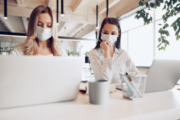 Deux collègues féminines travaillant ensemble au bureau portant des masques médicaux