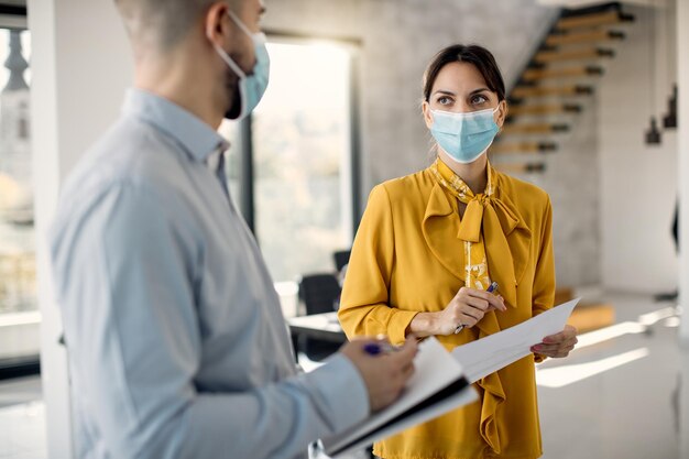 Deux collègues de travail avec des masques faciaux parlant au bureau