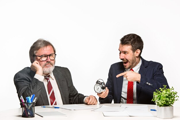 Les deux collègues travaillant ensemble au bureau sur fond blanc. Ils discutent activement et émotionnellement des plans actuels avec l'horloge