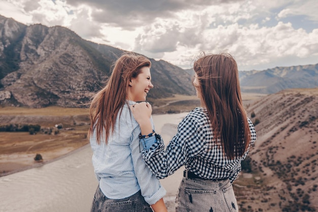 Deux copines amusantes passent du temps ensemble en pleine nature parmi les montagnes rocheuses et un ruisseau qui coule non loin de là. se regarder et rire bruyamment.