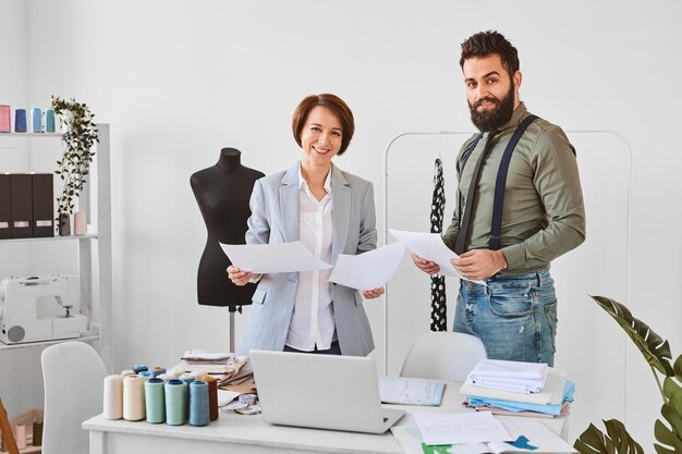 Deux créateurs de mode posant en atelier avec des plans de ligne de vêtements