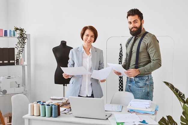 Deux créateurs de mode posant en atelier avec des plans de ligne de vêtements