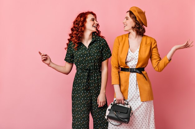 Deux dames de bonne humeur se regardant. Photo de Studio de filles raffinées parlant sur fond rose.