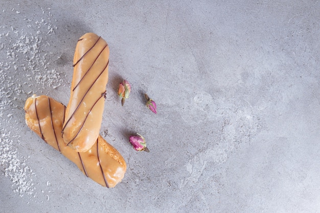 Deux éclairs remplis de caramel et de roses sur fond de pierre.