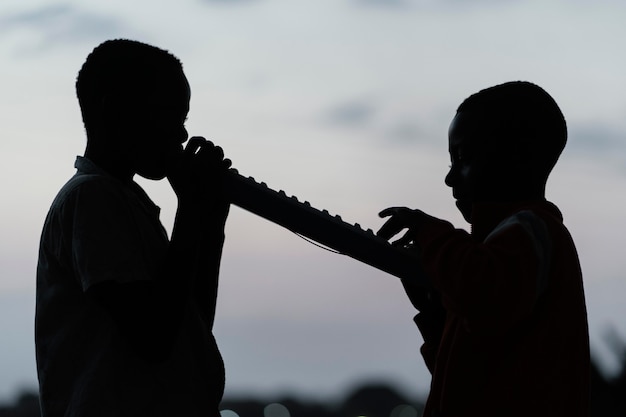 Photo gratuite deux enfants africains au coucher du soleil jouant de l'instrument