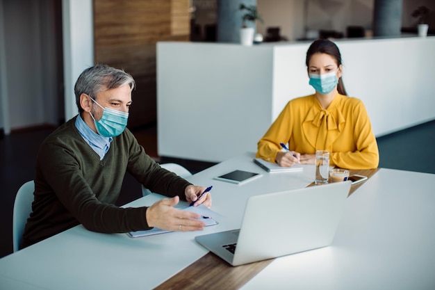 Deux entrepreneurs coopérant travaillant sur un ordinateur portable au bureau pendant la pandémie de coronavirus