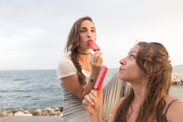 Deux femmes assises sur la côte en dégustant des sucettes rouges
