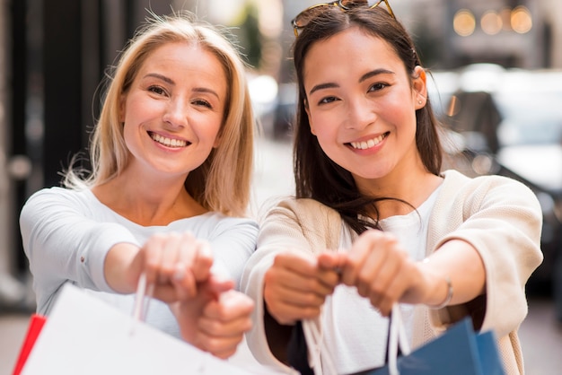 Photo gratuite deux femmes montrant des sacs à provisions défocalisés après une virée shopping