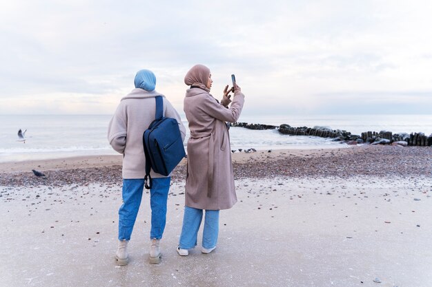 Deux femmes musulmanes prenant des photos avec un smartphone sur la plage lors d'un voyage