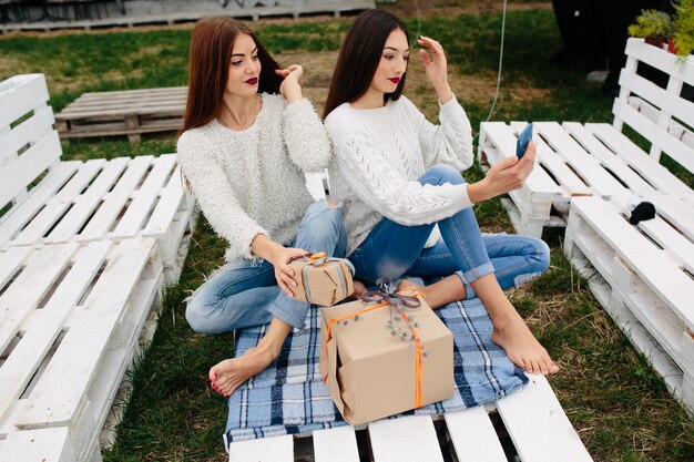 Deux femmes s'assoient sur un banc à l'extérieur et tirent des cadeaux pour smartphone