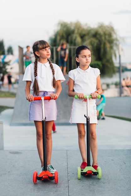 Deux, Filles, Debout, Sur, Rouge, Et, Vert, Pousser, Scooter, Dans Parc